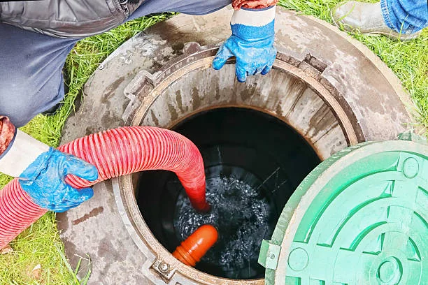 Technician pumping a residential septic tank through an open access lid.