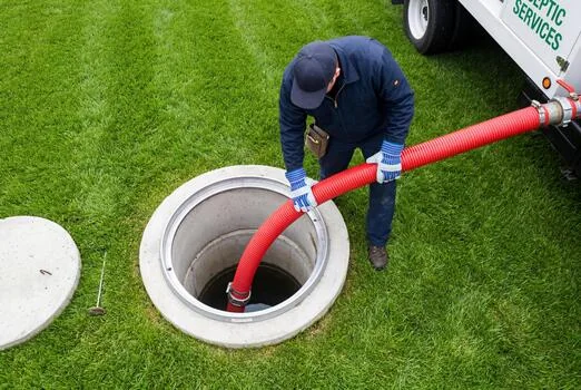 Septic service technician placing a pumping hose into an open septic tank.